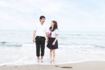 Young couple wearing school uniform standing on sandy beach — Stock Photo