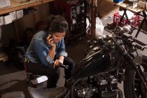 Mécanicien féminin utilisant le téléphone portable en atelier — Photo de stock