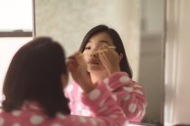 Jeune femme appliquant le maquillage en utilisant miroir de salle de bains — Photo de stock