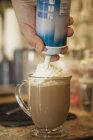Nahaufnahme des Kellners, der Schlagsahne auf eine Tasse heiße Schokolade spritzt — Stockfoto
