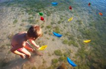 Хлопчик плаває паперовими човнами на пляжі — стокове фото