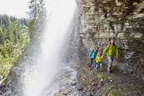 Young family, walking underneath waterfall — Stock Photo