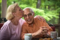 Senior mulher beijando homem, sorrindo — Fotografia de Stock