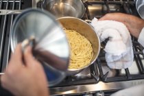 Повар поднимает крышку на кастрюлю спагетти на плите, возвышенный вид — стоковое фото