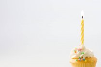 Bougie d'anniversaire sur cupcake décoré de crème et saupoudrer — Photo de stock