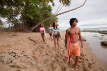Quatre jeunes amis portant des planches de surf sur la plage — Photo de stock