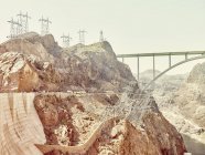 Face rocheuse de vallée avec pont éloigné et pylônes — Photo de stock