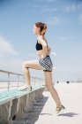 Metà donna adulta in spiaggia, facendo stretches sulla panchina, guardando la vista — Foto stock