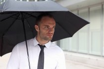 Porträt eines Geschäftsmannes, der unter einem Regenschirm wandelt — Stockfoto