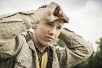 Low angle portrait of young man putting on flat cap looking away — Stock Photo