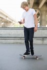 Мальчик-подросток на скейтборде с мобильным телефоном — стоковое фото