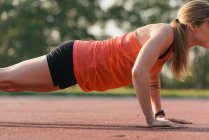 Young woman working out, doing press-ups, outdoors, mid section — Stock Photo