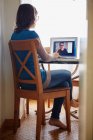 Jovem mulher sentada à mesa, usando laptop, em chamada de vídeo com mulher madura, visão traseira — Fotografia de Stock