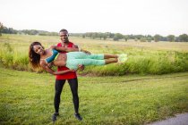 Young man training holding up girlfriend horizontally — Stock Photo