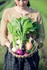 Молода жінка в полі тримає кошик з домашніми овочами — стокове фото