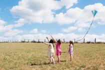 Tres chicas volando cometa en el campo - foto de stock