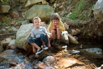 Chicos sentados en roca por río - foto de stock