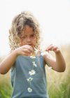 Junges Mädchen macht eine Gänseblümchenkette — Stockfoto