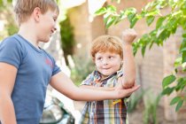 Boy feeling brothers biceps outdoors — Stock Photo