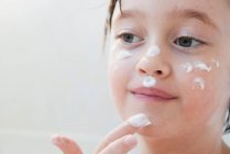 Chica frotando crema hidratante en su cara - foto de stock