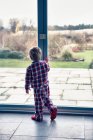 Rapaz de pijama a olhar pela janela — Fotografia de Stock