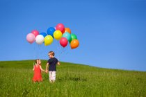 Дети с разноцветными воздушными шарами в траве — стоковое фото