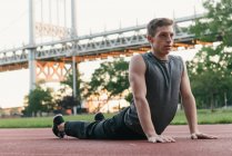 Young man on sports track, stretching — Stock Photo