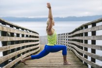 Portrait of young woman practicing yoga warrior pose on wooden pier — Stock Photo