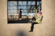 Architecte femme assise sur un cadre de fenêtre sur un chantier de construction — Photo de stock