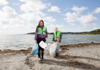 Meninas em coletes de segurança praia de limpeza — Fotografia de Stock