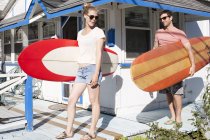 Couple on patio carrying surfboards, Breezy Point, Queens, New York, USA — Stock Photo
