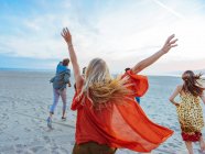 Группа друзей, идущих вдоль пляжа, молодая женщина с руками в воздухе, вид сзади — стоковое фото
