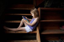 Kleines Mädchen sitzt auf Kellertreppe und blickt auf digitales Tablet — Stockfoto