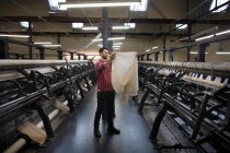 Portrait of male weaver examining cloth from old weaving machine in textile mill — Stock Photo