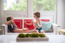 Ragazzo e ragazza sul divano conservatorio con pacchetti di patatine — Foto stock