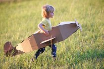 Мальчик летит на картонном самолете на открытом воздухе, сосредоточиться на переднем плане — стоковое фото