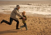 Жінка біжить грати з хлопчиком на пляжі — стокове фото