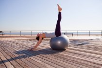 Frau dehnt sich auf Gymnastikball auf Promenade — Stockfoto