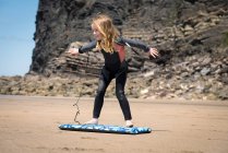 Girl in wetsuit playing with surfboard — Stock Photo