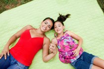 Мати і дочка лежать на ковдрі, тримаючись за руки — стокове фото