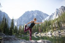 Young woman standing on rock beside lake, in yoga pose, The Enchantments, Alpine Lakes Wilderness, Washington, USA — Stock Photo