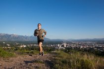 Joven corredor masculino corriendo por la pista por encima de la ciudad en el valle - foto de stock