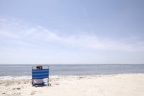 Chica mirando por encima de su hombro desde la silla de cubierta en la playa - foto de stock