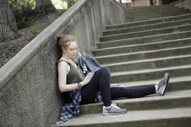 Молодая женщина сидит одна на лестнице и слушает музыку в наушниках — стоковое фото