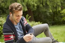 Ritratto di uomo disteso in giardino ad ascoltare smartphone che indossa auricolari — Foto stock
