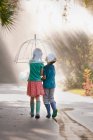 Rear view of boy and girl carrying umbrella on street — Stock Photo