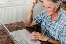 Uomo più anziano utilizzando il computer portatile in cucina — Foto stock