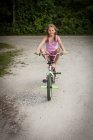 Vista frontal da menina equilibrando na bicicleta, pernas levantadas, olhando para a câmera sorrindo — Fotografia de Stock