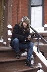 Jovem homem lendo texto no smartphone na neve coberto porta da frente passo — Fotografia de Stock