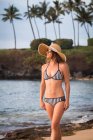 Femme adulte moyenne portant un chapeau de soleil et un bikini se promenant sur la plage, Maui, Hawaï, États-Unis — Photo de stock